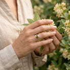 [KI] Silberring mit Tigerauge an der Hand zwischen Blumen