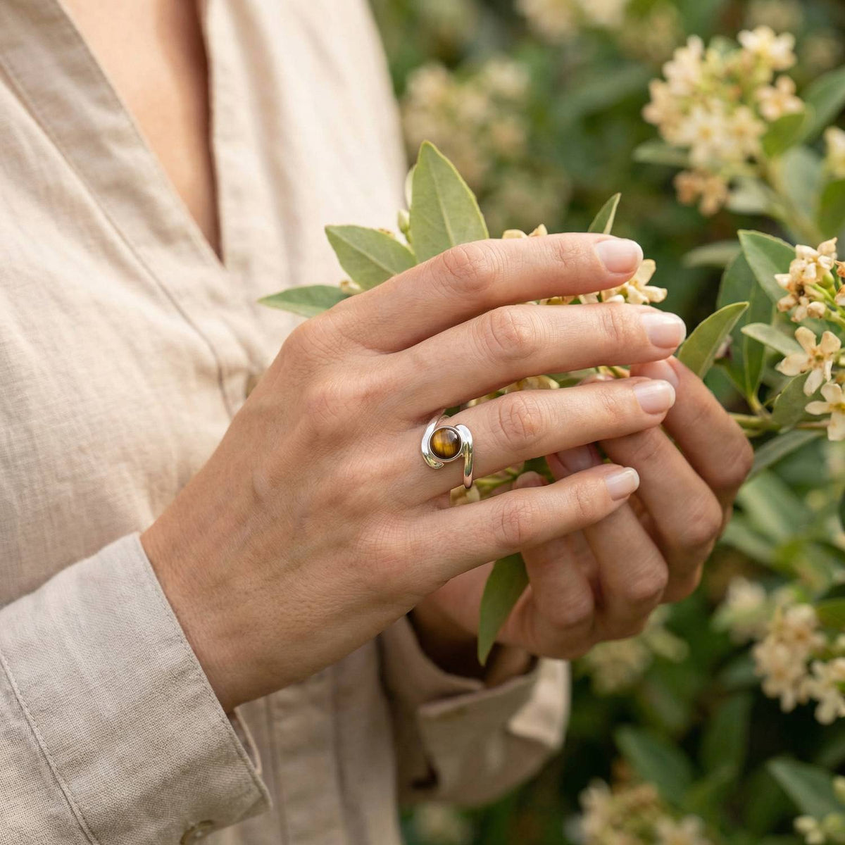 Silberring mit Tigerauge an der Hand zwischen Blumen