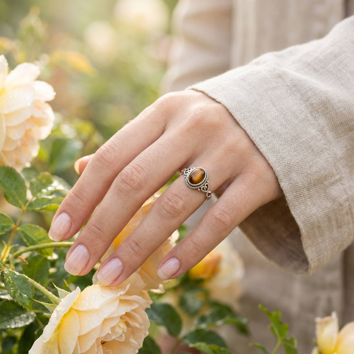 Silberring mit Tigerauge an der Hand zwischen Blumen