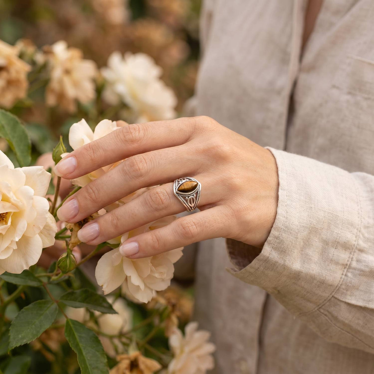Silberring mit Tigerauge an der Hand zwischen Blumen