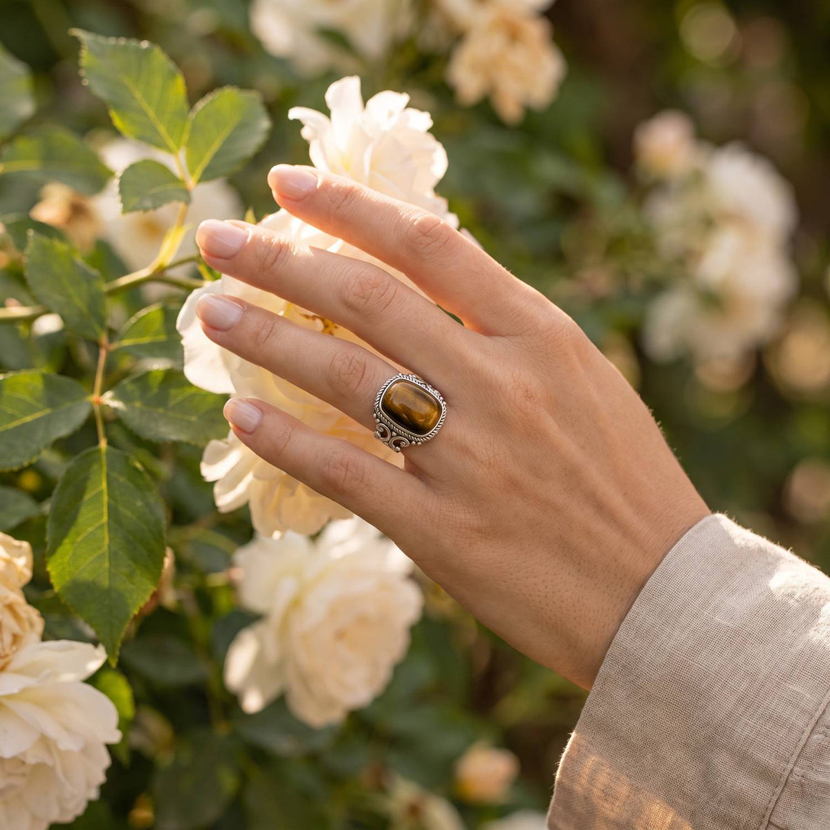 Silberring mit Tigerauge an der Hand zwischen Blumen