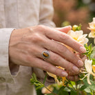 [KI] Silberring mit Tigerauge an der Hand zwischen Blumen