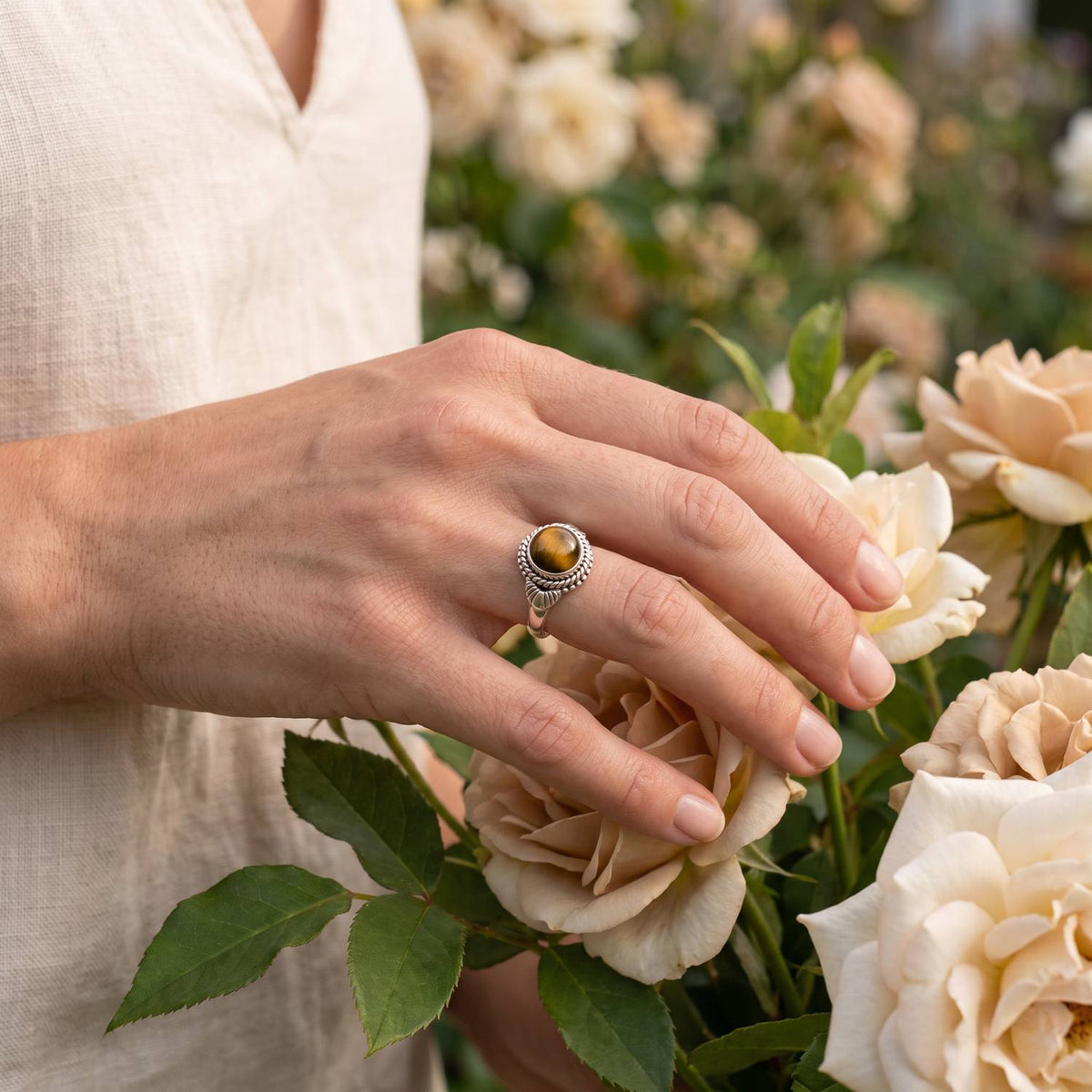 Silberring mit Tigerauge an der Hand zwischen Blumen