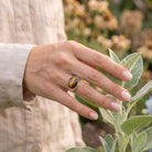 [KI] Silberring mit Tigerauge an der Hand zwischen Blumen