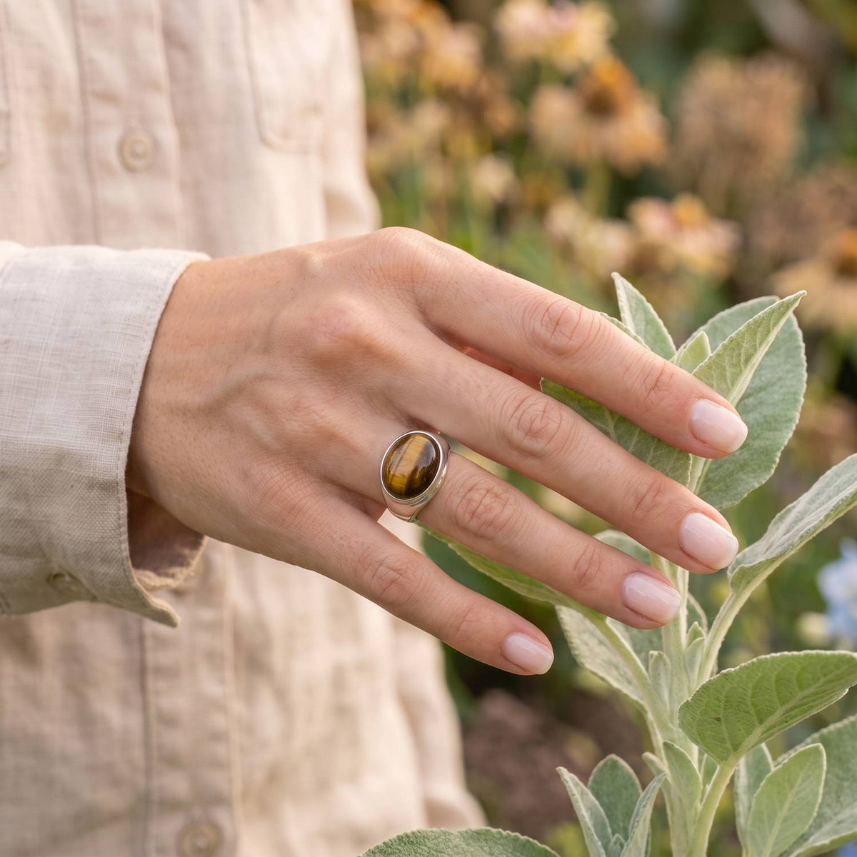 Silberring mit Tigerauge an der Hand zwischen Blumen