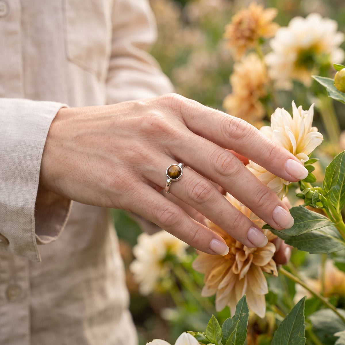 Silberring mit Tigerauge an der Hand zwischen Blumen
