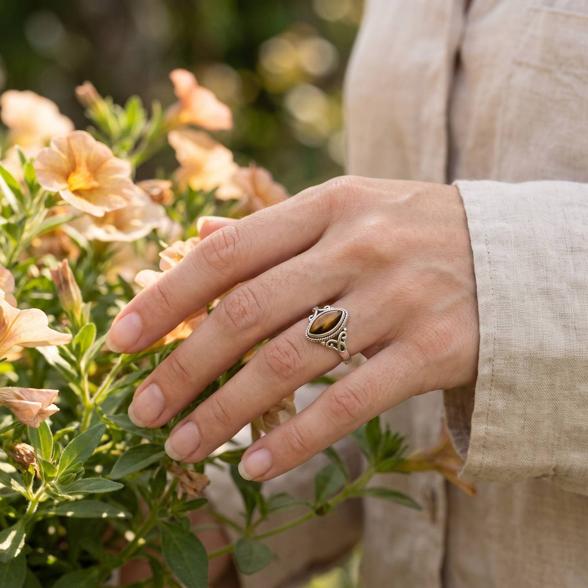 Silberring mit Tigerauge an der Hand zwischen Blumen