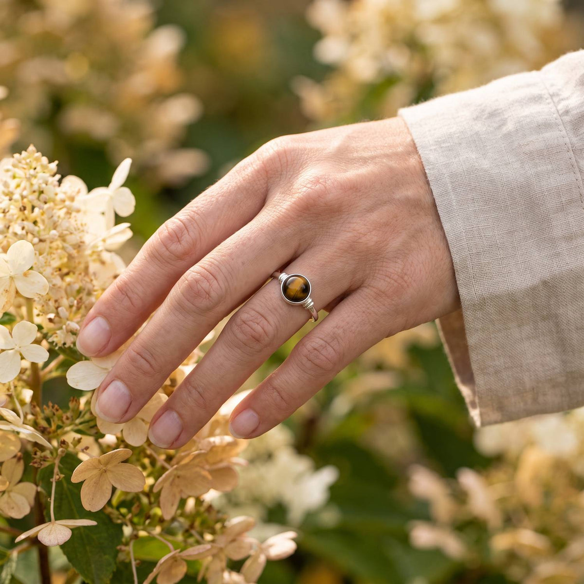 Silberring mit Tigerauge an der Hand zwischen Blumen