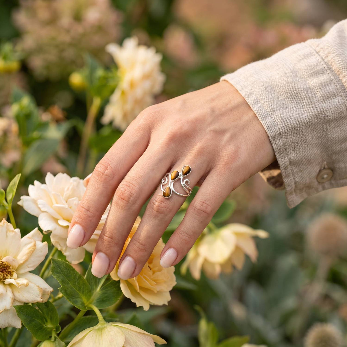 Silberring mit Tigerauge an der Hand zwischen Blumen