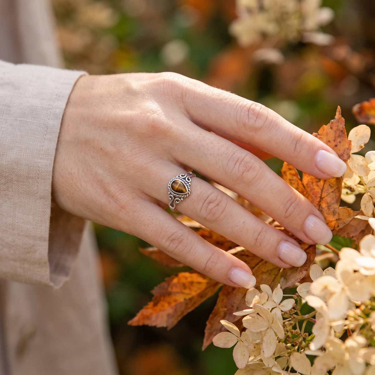 Silberring mit Tigerauge an der Hand zwischen Blumen