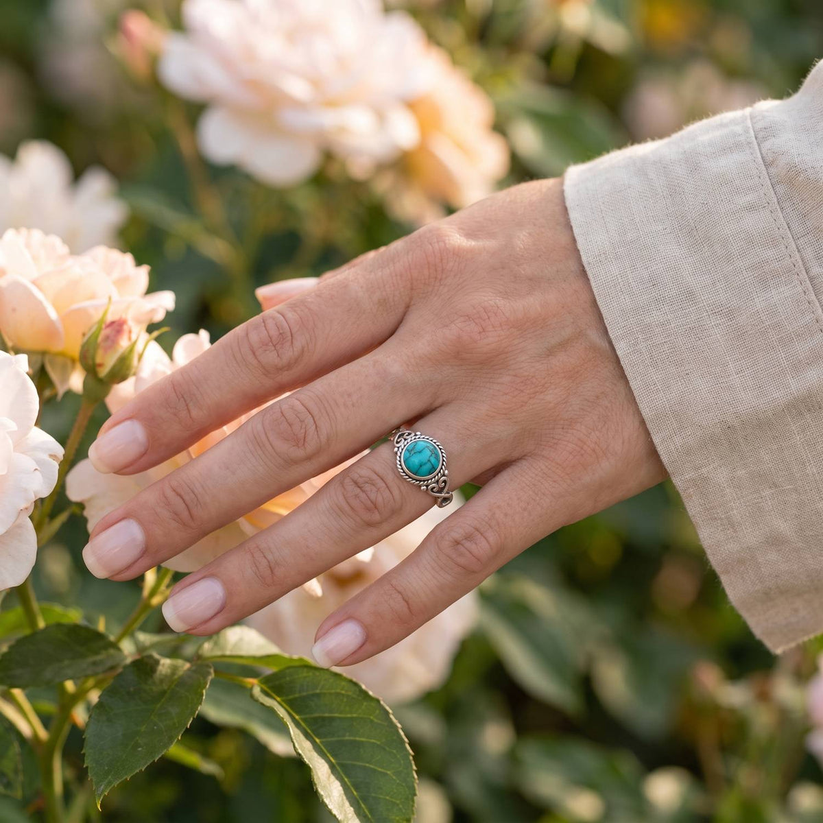 Silberring mit Türkis an der Hand zwischen Blumen