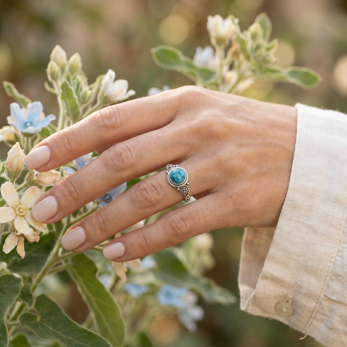 Silberring mit Türkis an der Hand zwischen Blumen
