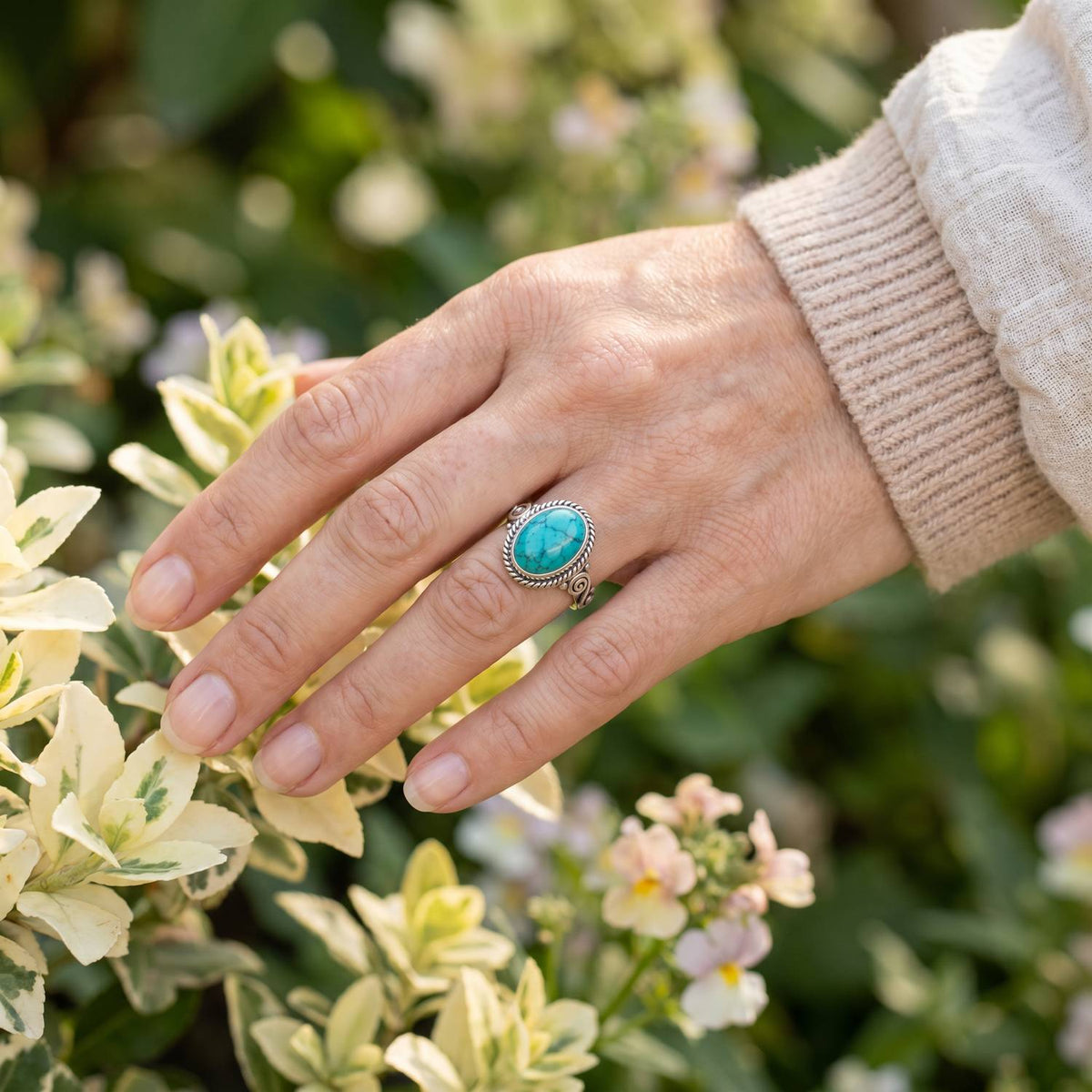 Silberring mit Türkis an der Hand zwischen Blumen