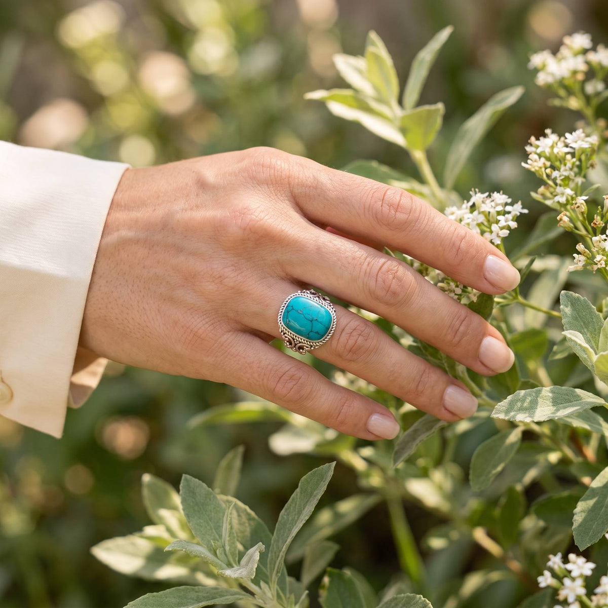 Silberring mit Türkis an der Hand zwischen Blumen