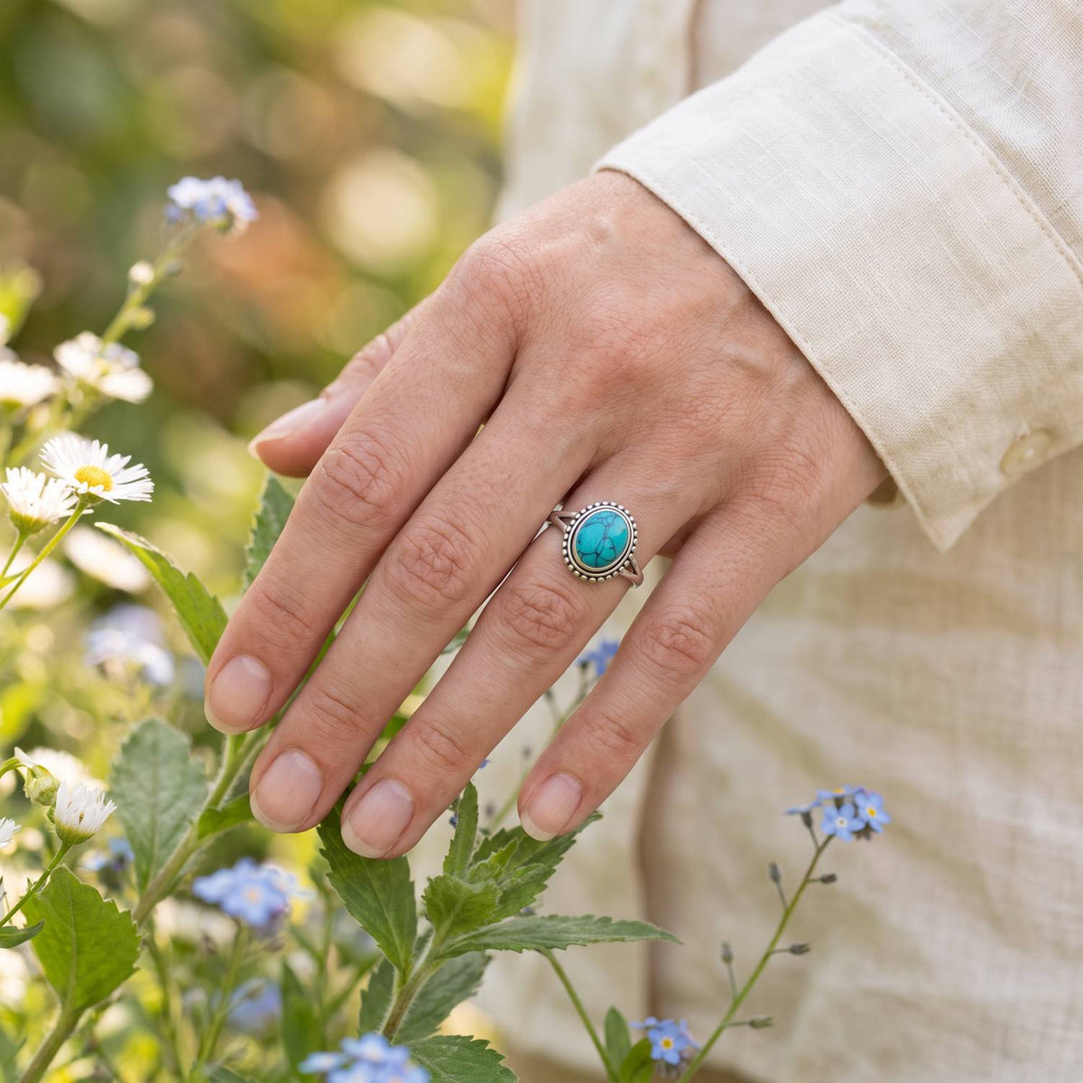 Silberring mit Türkis an der Hand zwischen Blumen