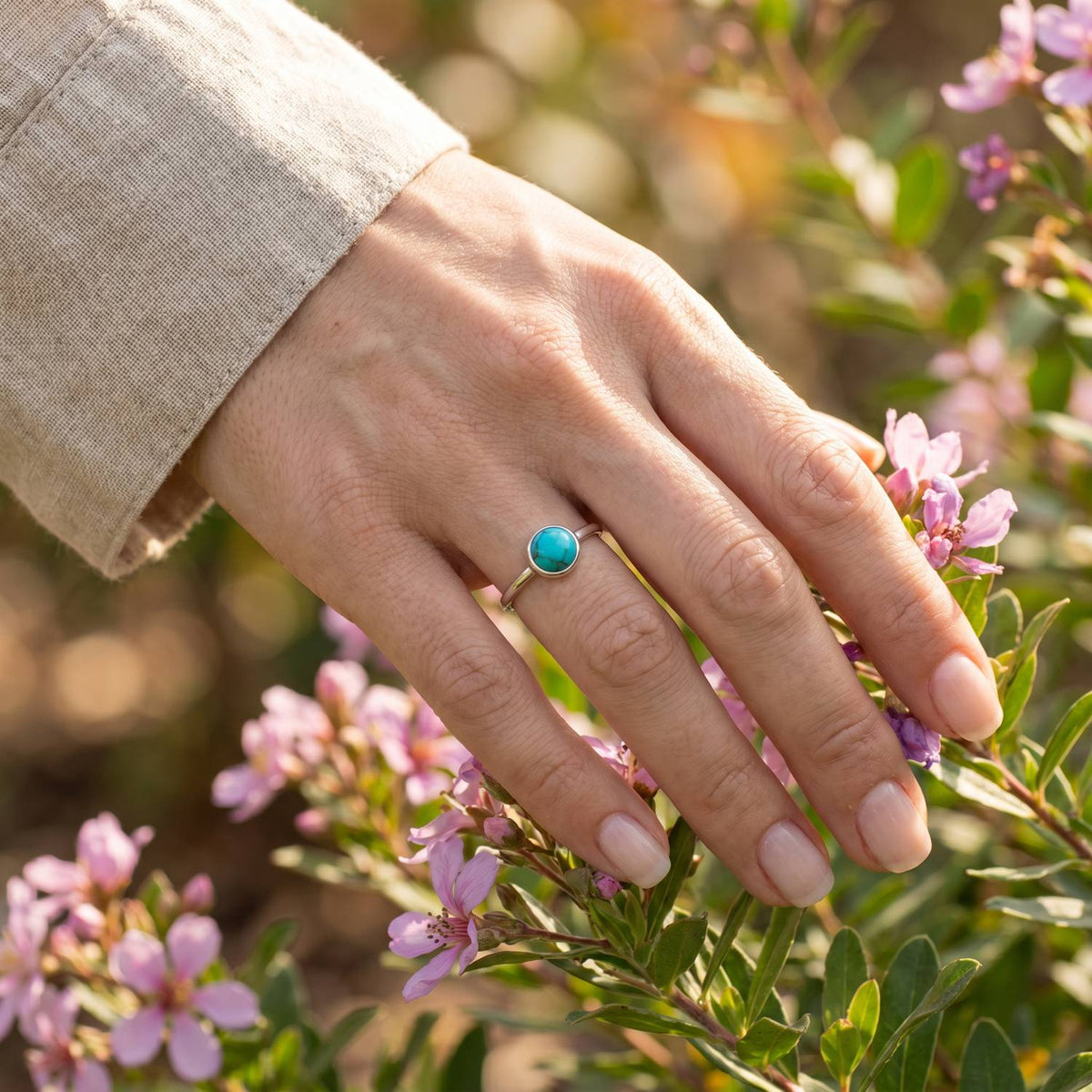 Silberring mit Türkis an der Hand zwischen Blumen