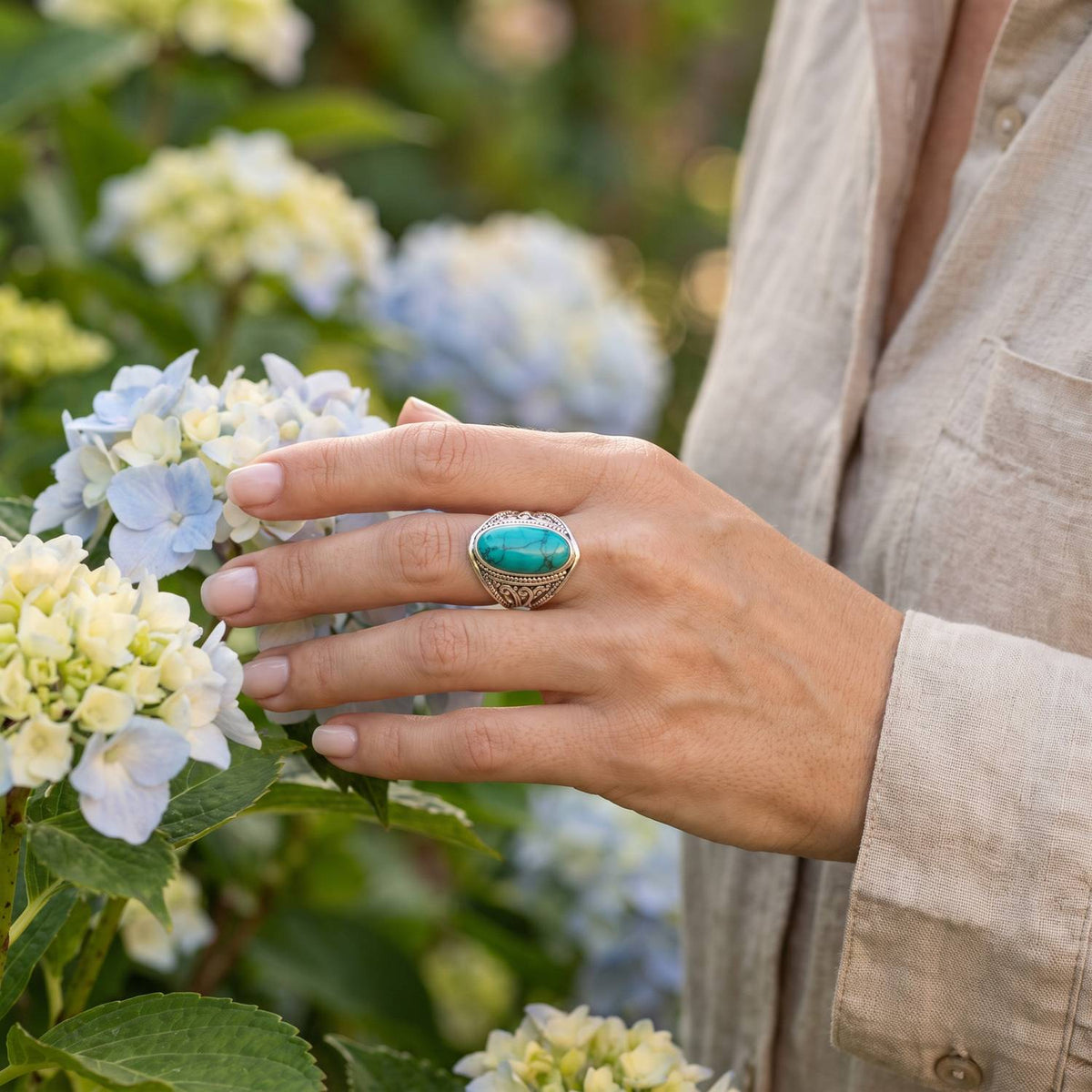 Silberring mit Türkis an der Hand zwischen Blumen