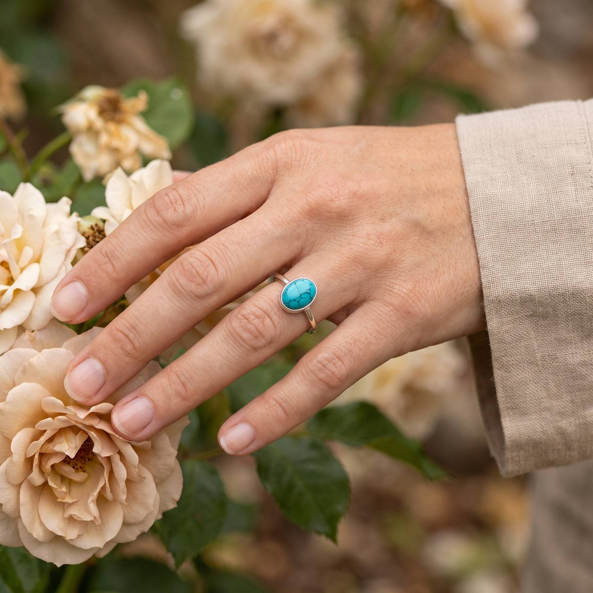 Silberring mit Türkis an der Hand zwischen Blumen