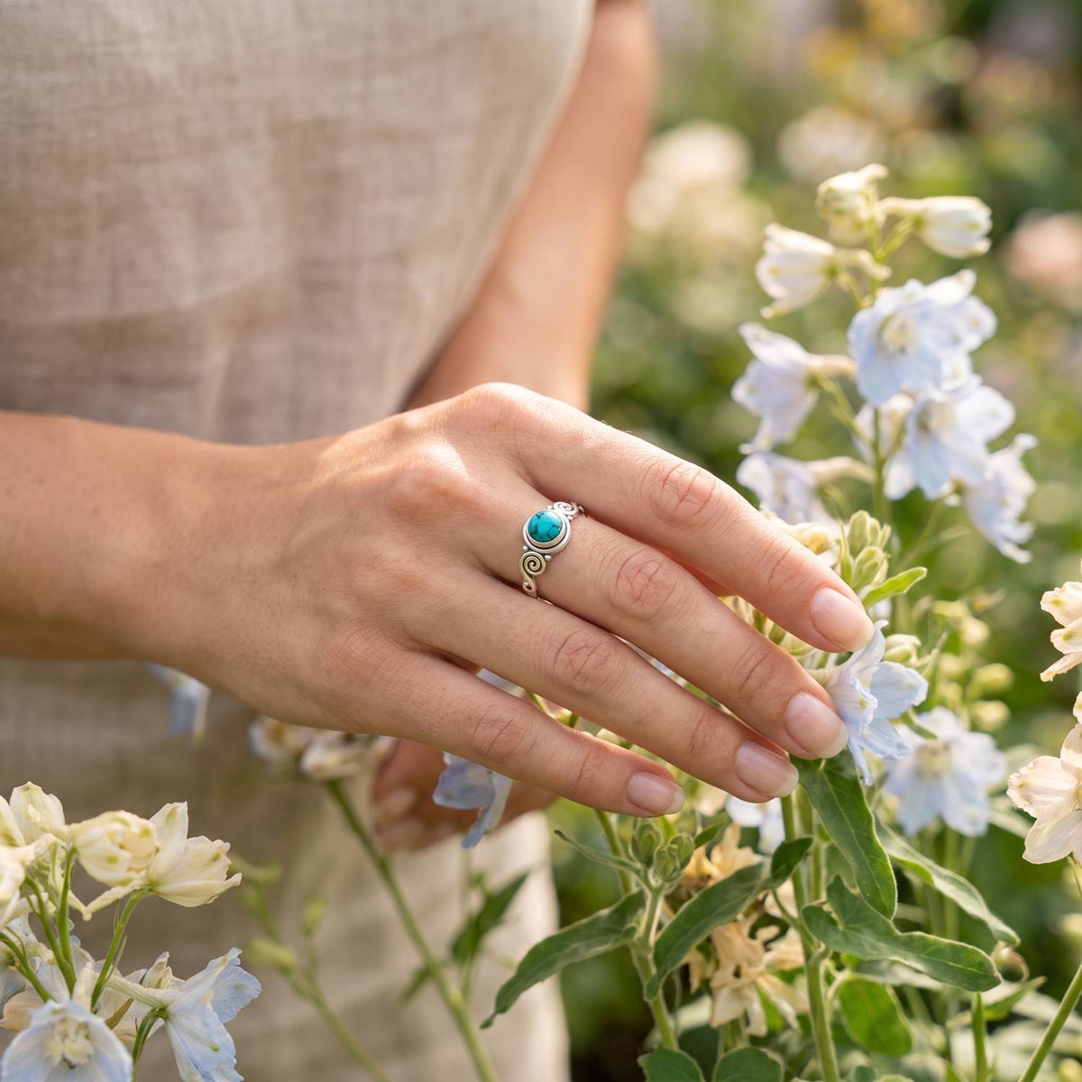 Silberring mit Türkis an der Hand zwischen Blumen