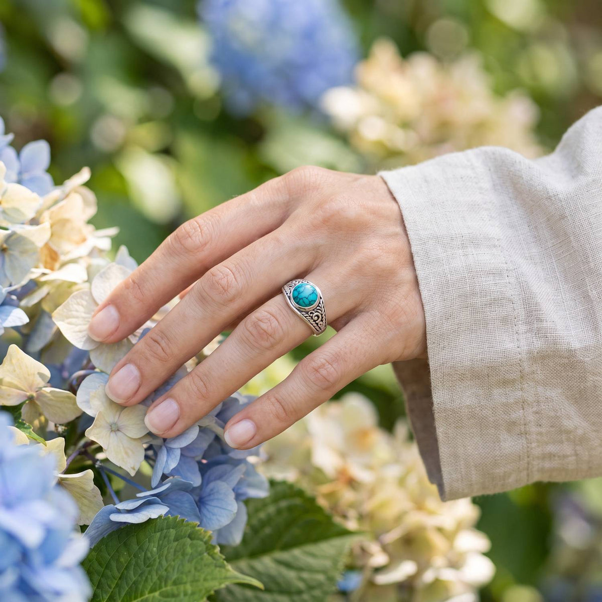 Silberring mit Türkis an der Hand zwischen Blumen