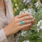 [KI] Silberring mit Türkis an der Hand zwischen Blumen