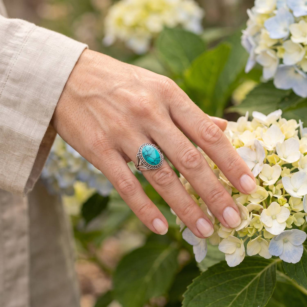 Silberring mit Türkis an der Hand zwischen Blumen
