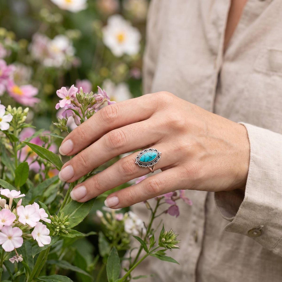 Silberring mit Türkis an der Hand zwischen Blumen