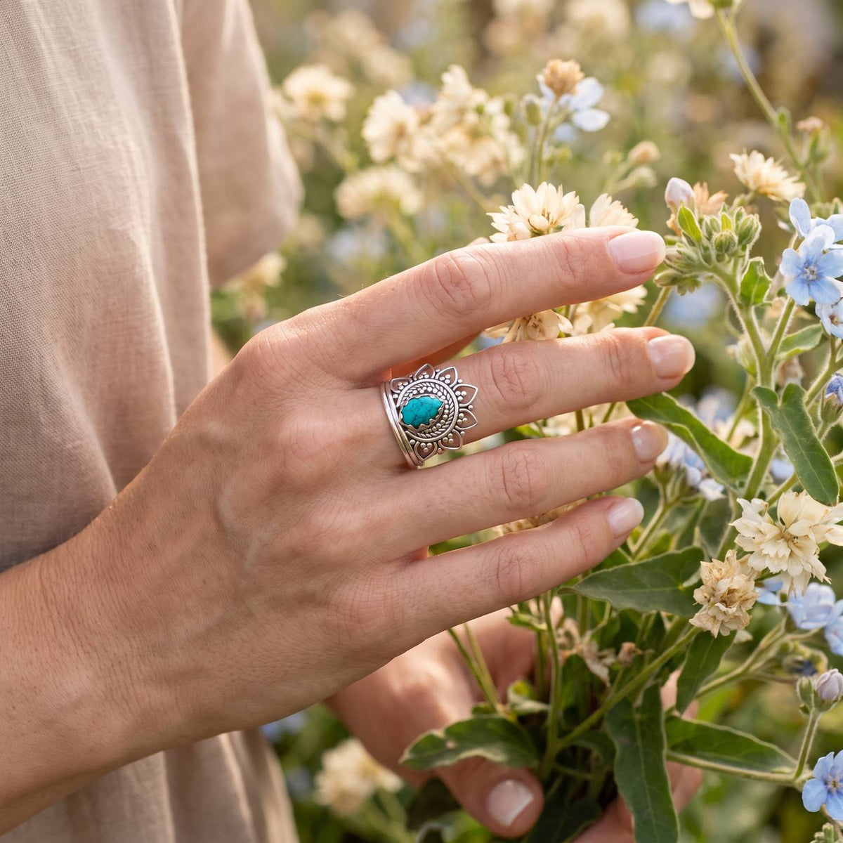 Silberring mit Türkis an der Hand zwischen Blumen