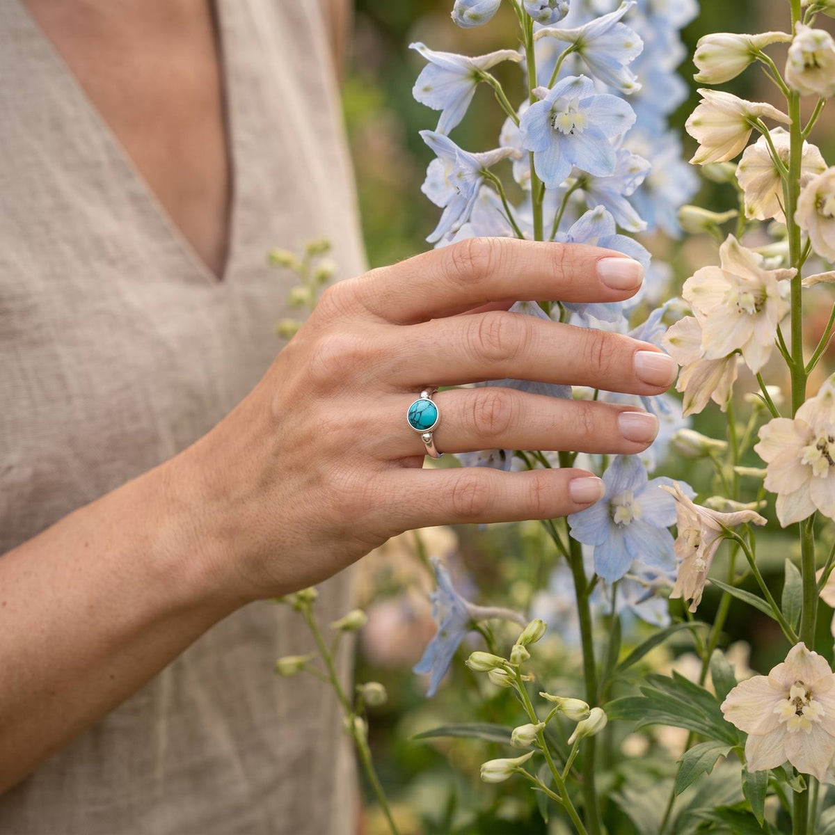Silberring mit Türkis an der Hand zwischen Blumen