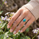 [KI] Silberring mit Türkis an der Hand zwischen Blumen