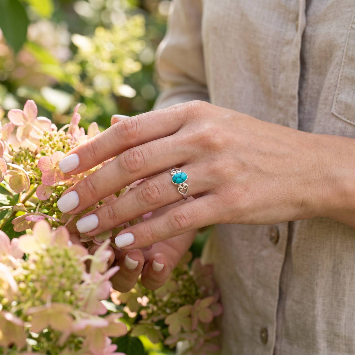 Silberring mit Türkis an der Hand zwischen Blumen