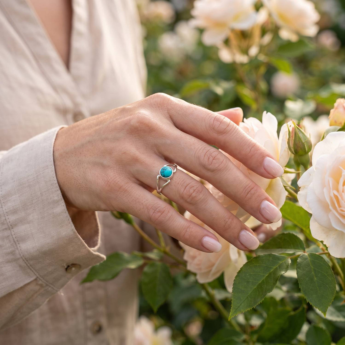 Silberring mit Türkis an der Hand zwischen Blumen