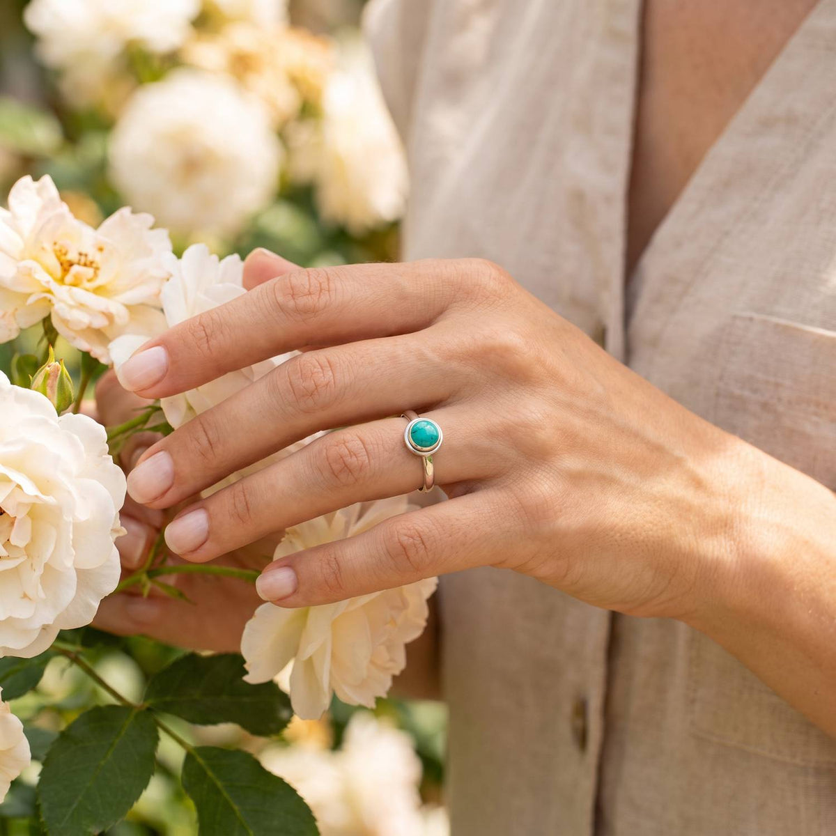 Silberring mit Türkis an der Hand zwischen Blumen