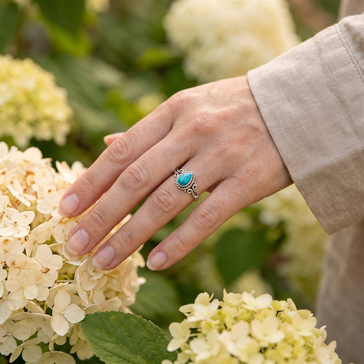 Silberring mit Türkis an der Hand zwischen Blumen