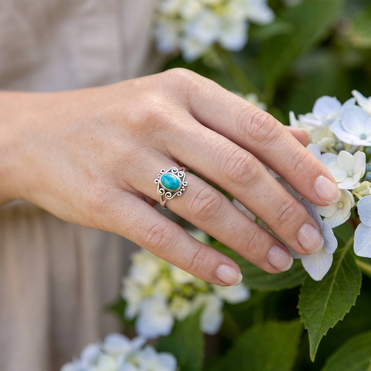 Silberring mit Türkis an der Hand zwischen Blumen