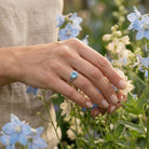 [KI] Silberring mit Topas an der Hand zwischen Blumen