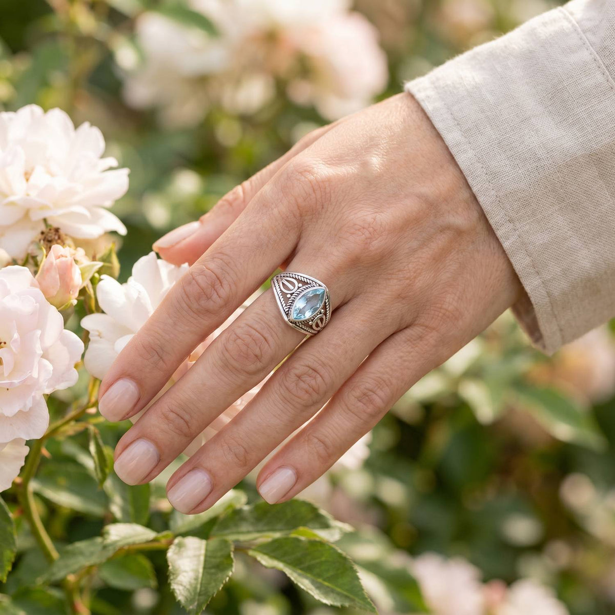 Silberring mit Topas an der Hand zwischen Blumen