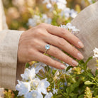 [KI] Silberring mit Topas an der Hand zwischen Blumen