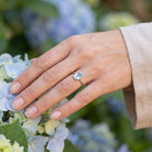 [KI] Silberring mit Topas an der Hand zwischen Blumen