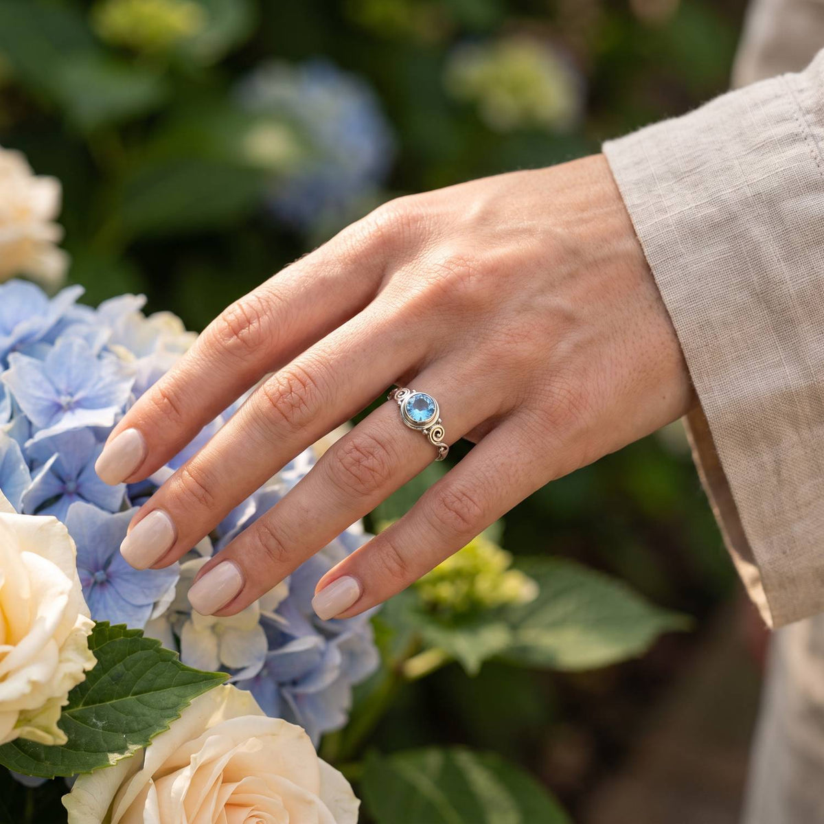 Silberring mit Topas an der Hand zwischen Blumen