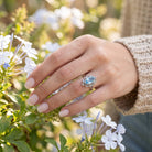 [KI] Silberring mit Topas an der Hand zwischen Blumen