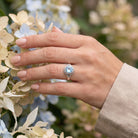 [KI] Silberring mit Topas an der Hand zwischen Blumen