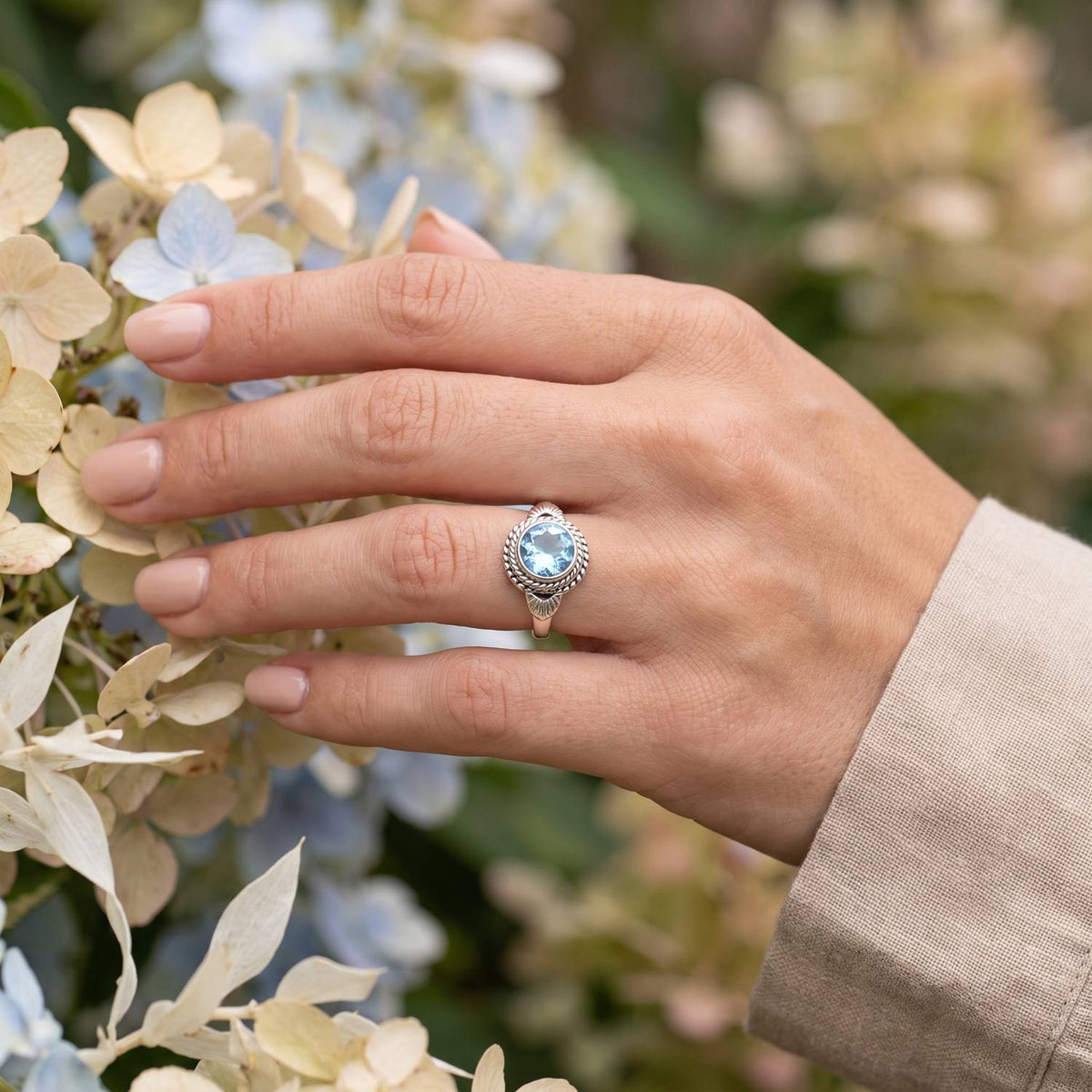 Silberring mit Topas an der Hand zwischen Blumen