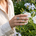 [KI] Silberring mit Topas an der Hand zwischen Blumen