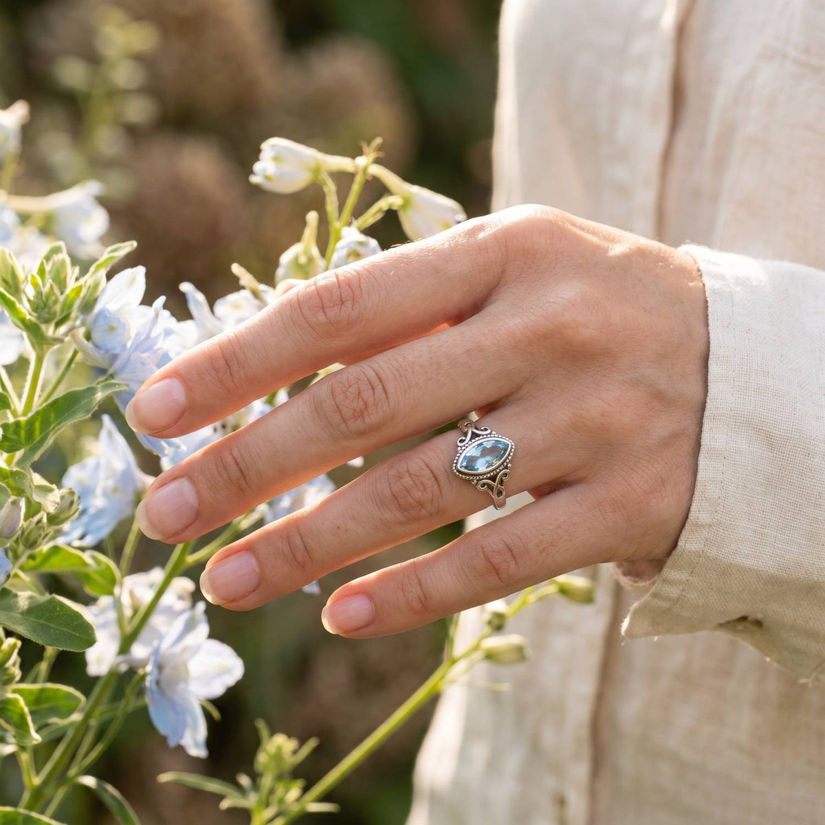 Silberring mit Topas an der Hand zwischen Blumen