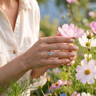 [KI] Silberring mit Topas an der Hand zwischen Blumen