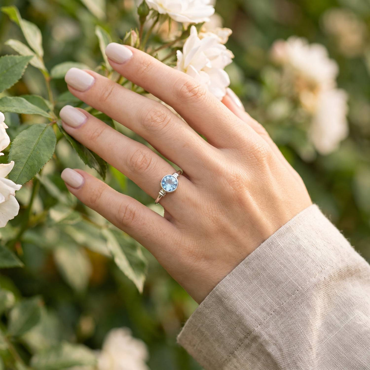 Silberring mit Topas an der Hand zwischen Blumen