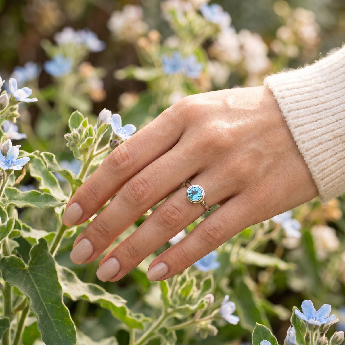 Silberring mit Topas an der Hand zwischen Blumen