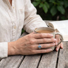 [KI] Topasring aus Silber getragen beim Lesen mit einer Tasse