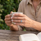 [KI] Topasring aus Silber getragen beim Lesen mit einer Tasse